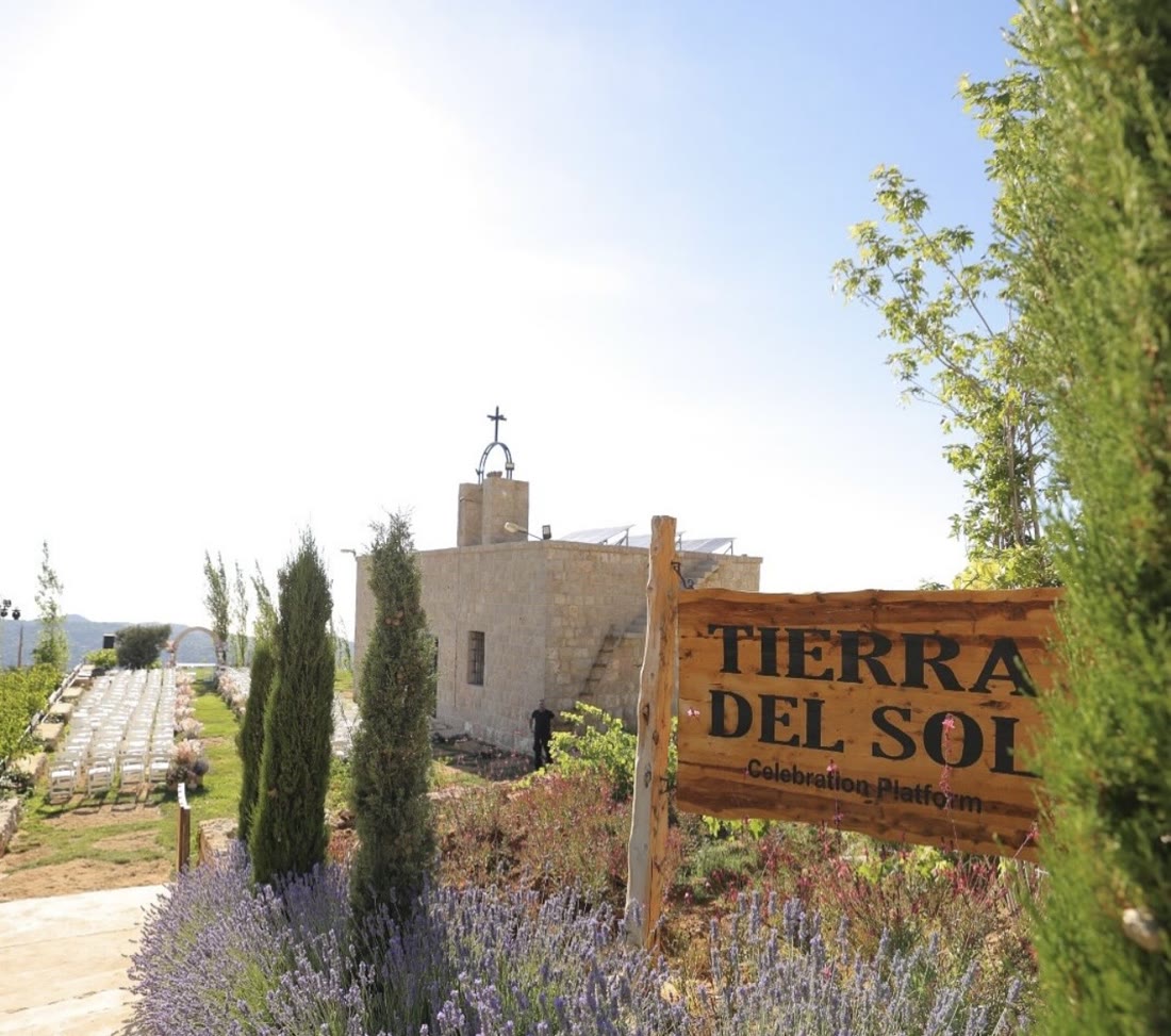 The carved wooden Tierra del Sol Celebration Platform sign beside the chapel and cypress trees.